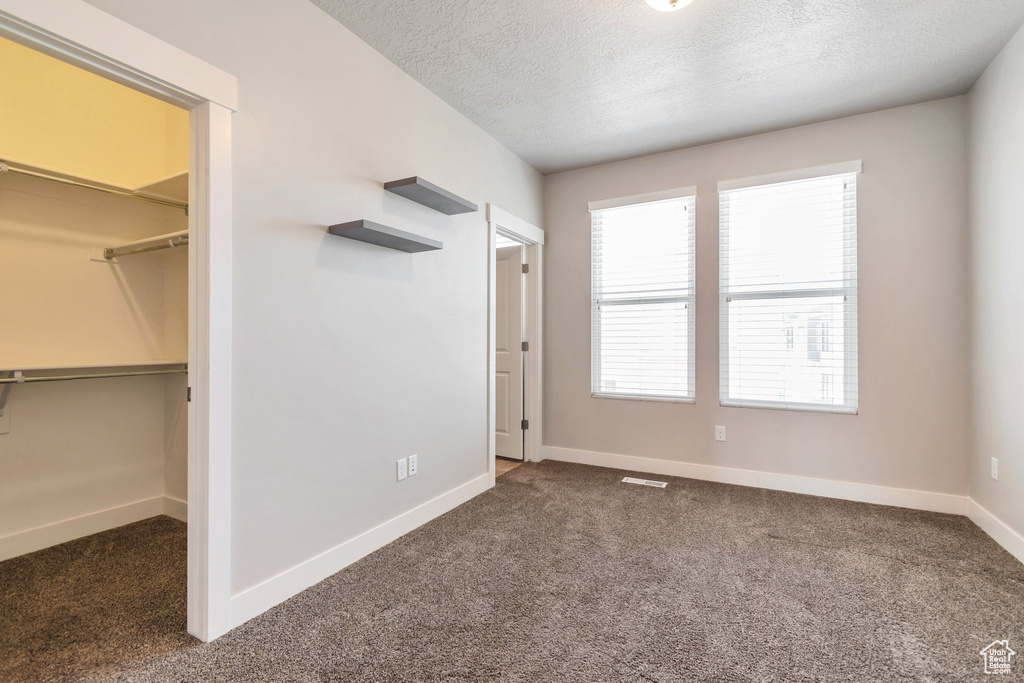 Unfurnished bedroom featuring a spacious closet, carpet, a textured ceiling, and a closet