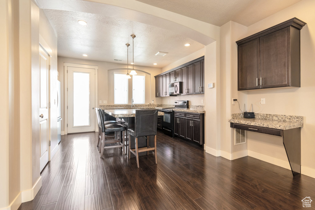 Kitchen with black electric range, stainless steel microwave, arched walkways, a breakfast bar, and dark brown cabinetry