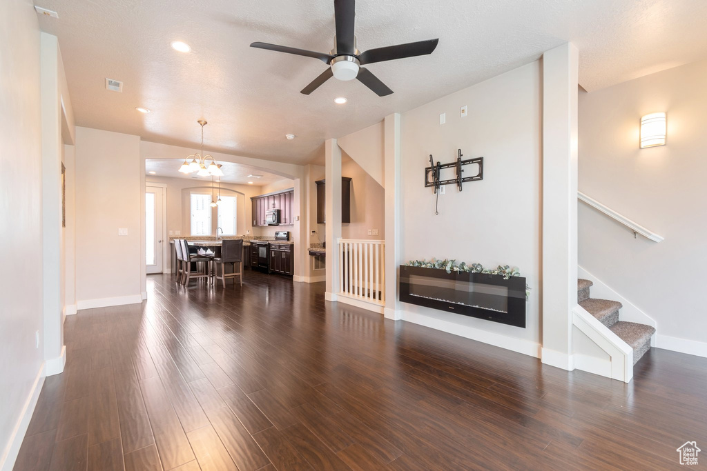 Living room with dark wood-style flooring, a ceiling fan, a chandelier, stairs, and recessed lighting