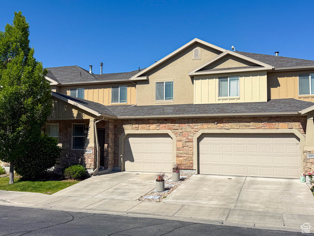 Townhome / multi-family property with driveway, stone siding, and a garage