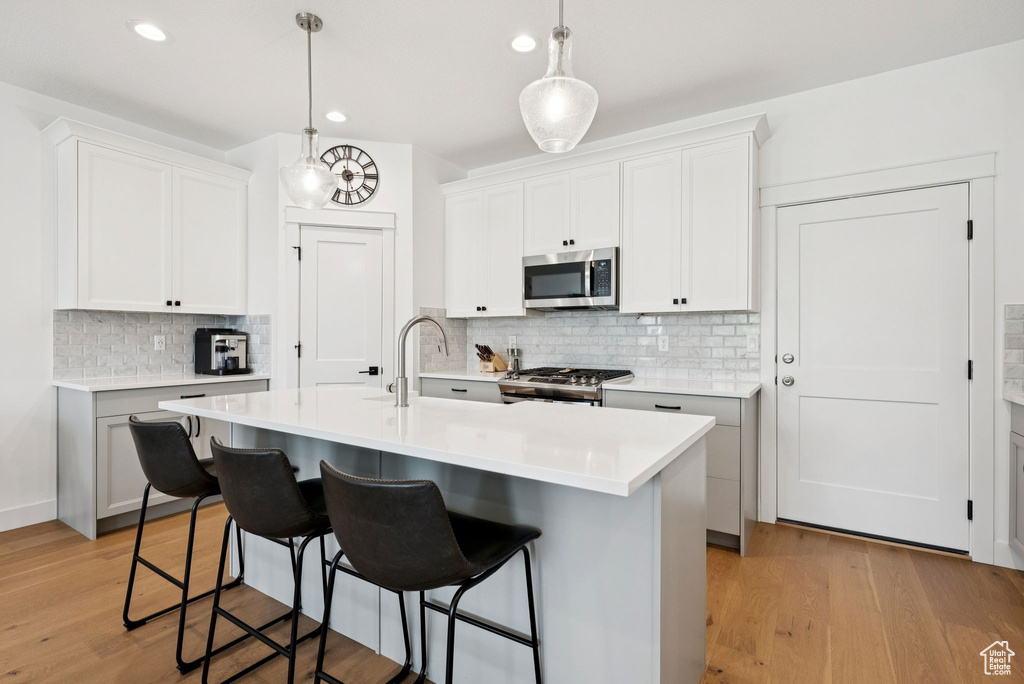 Kitchen with appliances with stainless steel finishes, decorative backsplash, a breakfast bar, light countertops, and light wood finished floors