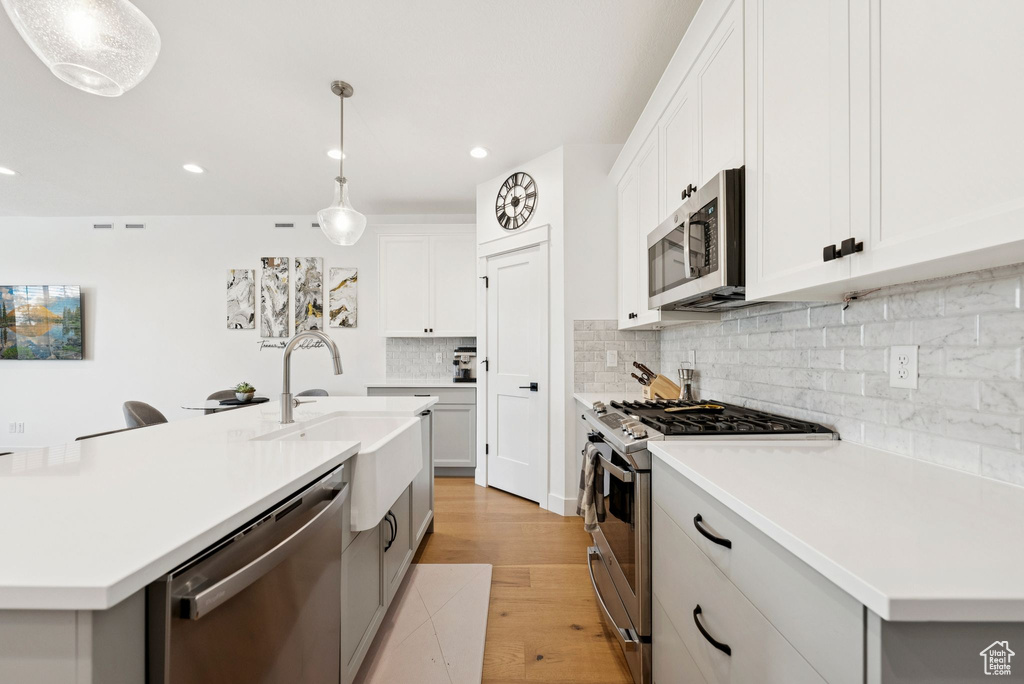 Kitchen featuring stainless steel appliances, light wood-style floors, light countertops, backsplash, and recessed lighting