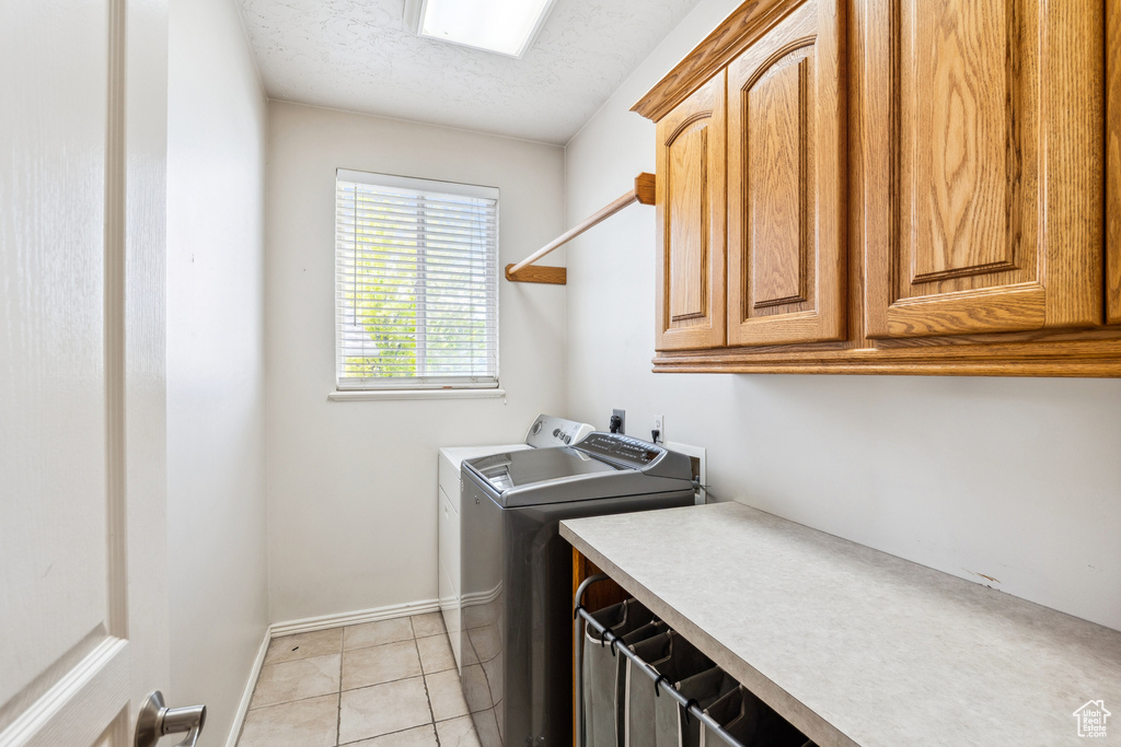 Laundry room with cabinet space, washing machine and dryer, a textured ceiling, and light tile patterned flooring