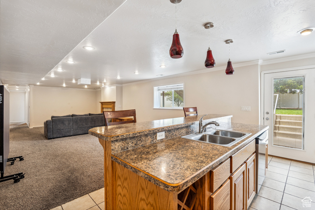 Kitchen with ornamental molding, light tile patterned floors, an island with sink, dishwasher, and decorative light fixtures