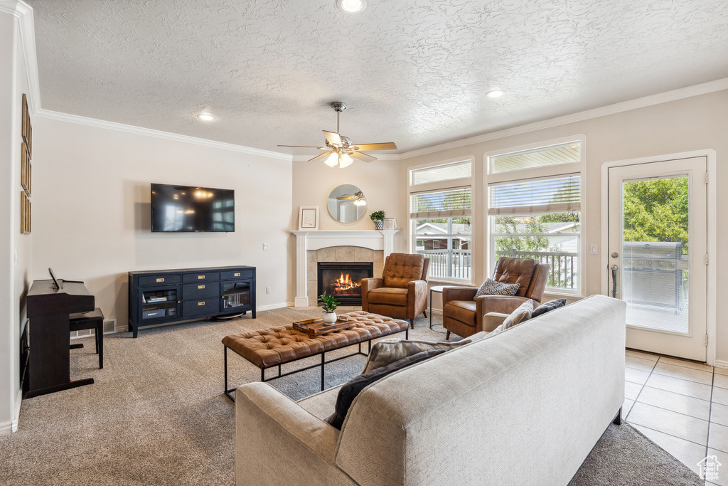 Living area featuring healthy amount of natural light, ceiling fan, a tiled fireplace, ornamental molding, and a textured ceiling
