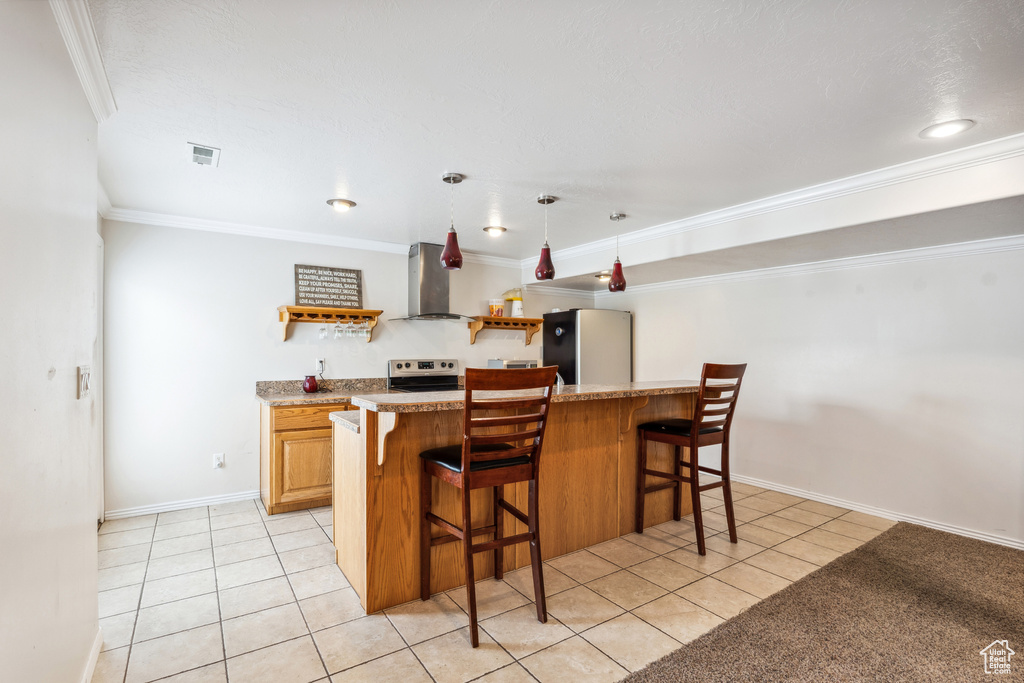 Kitchen featuring freestanding refrigerator, wall chimney exhaust hood, light tile patterned floors, a kitchen breakfast bar, and ornamental molding
