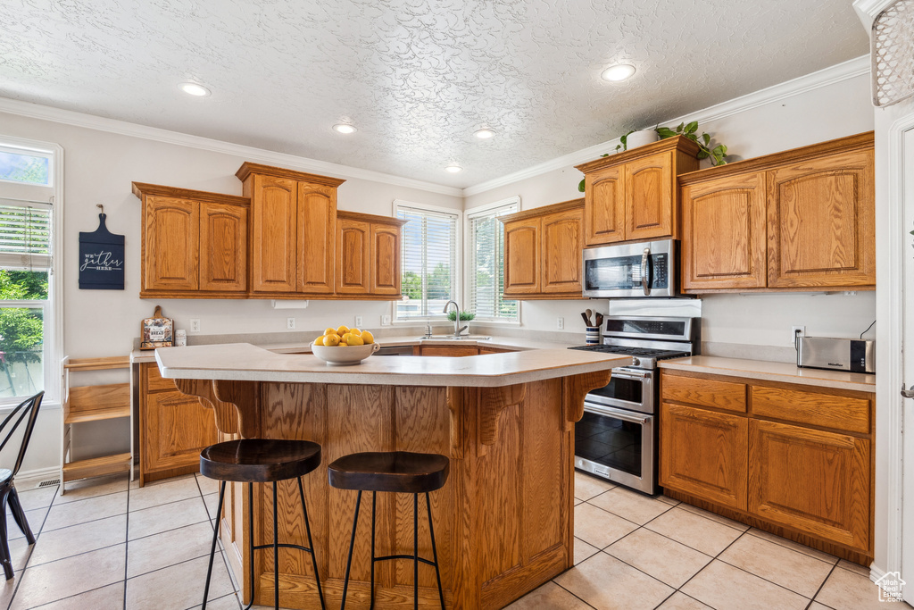 Kitchen with appliances with stainless steel finishes, healthy amount of natural light, a kitchen bar, light countertops, and a textured ceiling