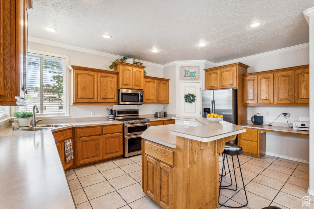 Kitchen featuring appliances with stainless steel finishes, light countertops, a kitchen breakfast bar, brown cabinets, and a center island