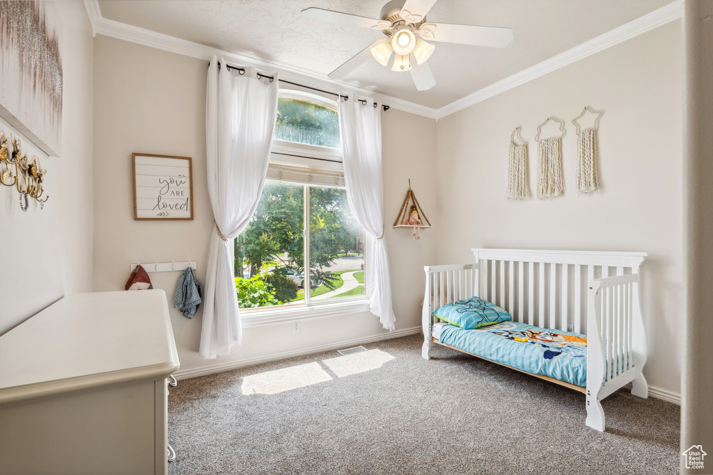 Carpeted bedroom with ornamental molding, ceiling fan, and a crib