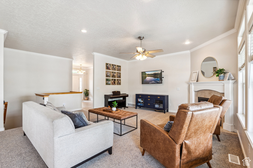 Living area with light colored carpet, ceiling fan, crown molding, a tiled fireplace, and a textured ceiling