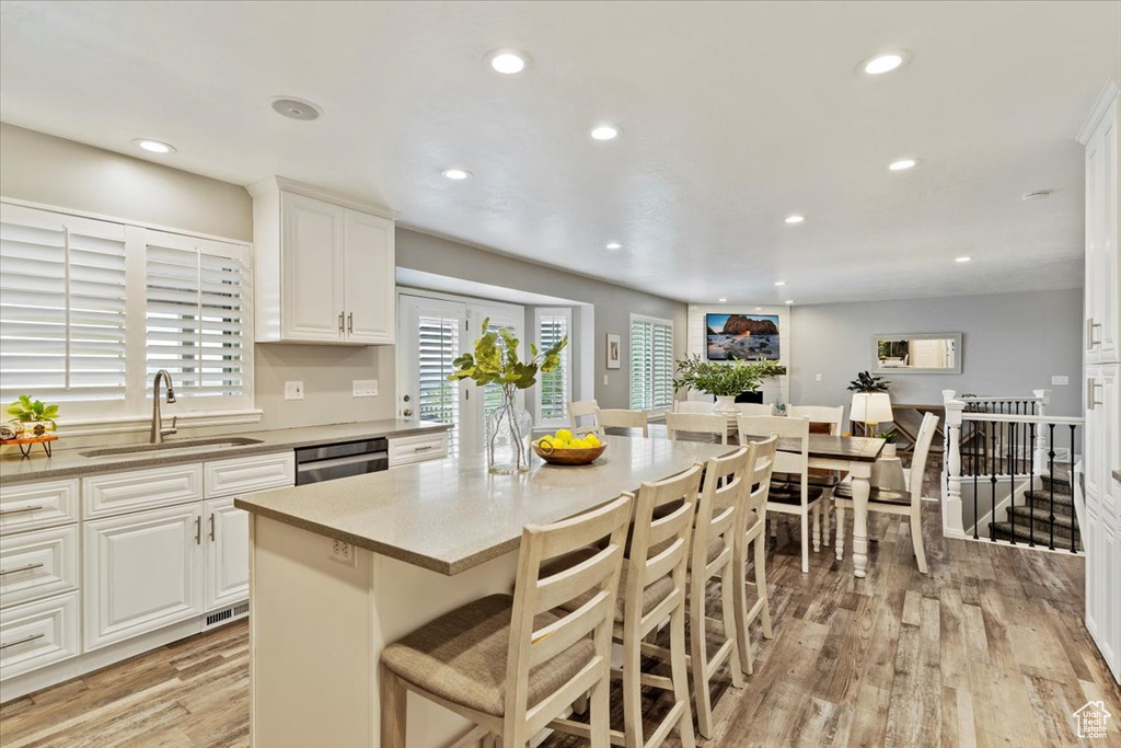 Kitchen with light wood finished floors, dishwasher, recessed lighting, a kitchen bar, and white cabinets