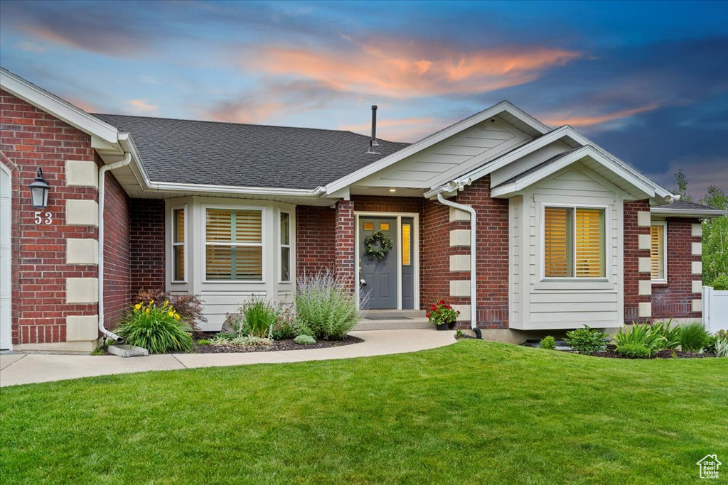 View of front of property with a yard, brick siding, and a shingled roof