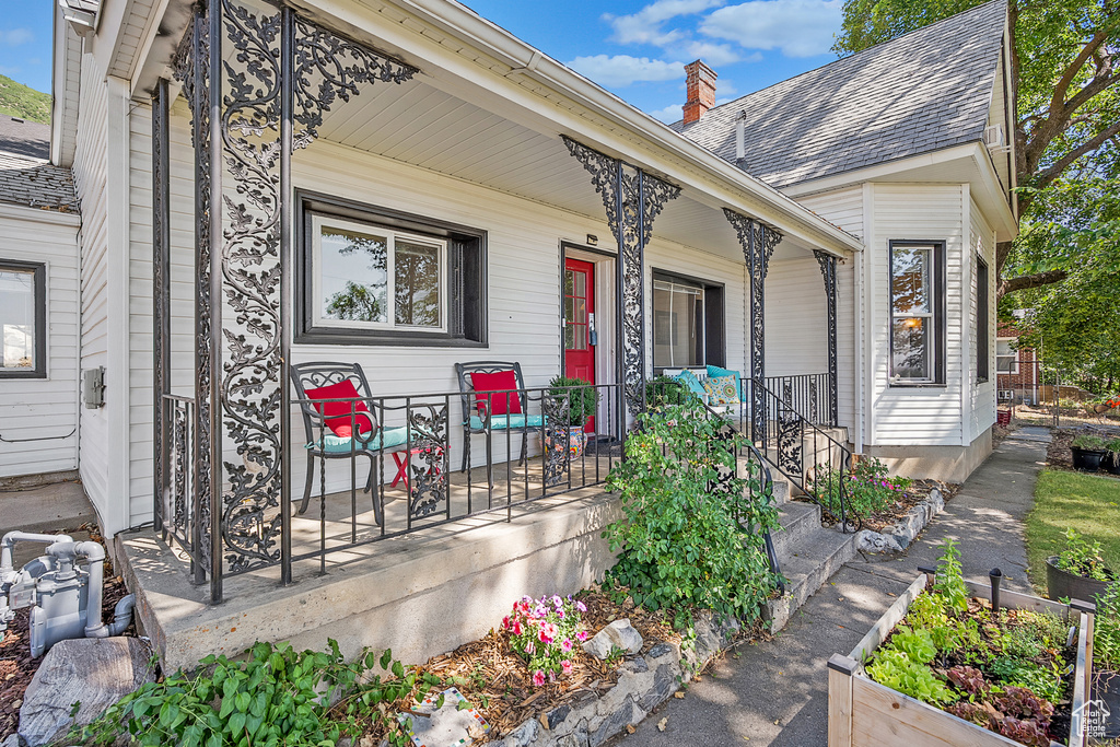 Entrance to property with covered porch, a chimney, and a shingled roof
