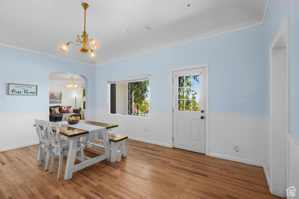 Dining room with a chandelier, arched walkways, a wainscoted wall, light wood finished floors, and crown molding