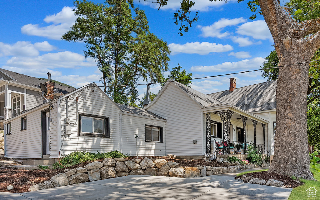View of front of property featuring covered porch, a chimney, and a shingled roof