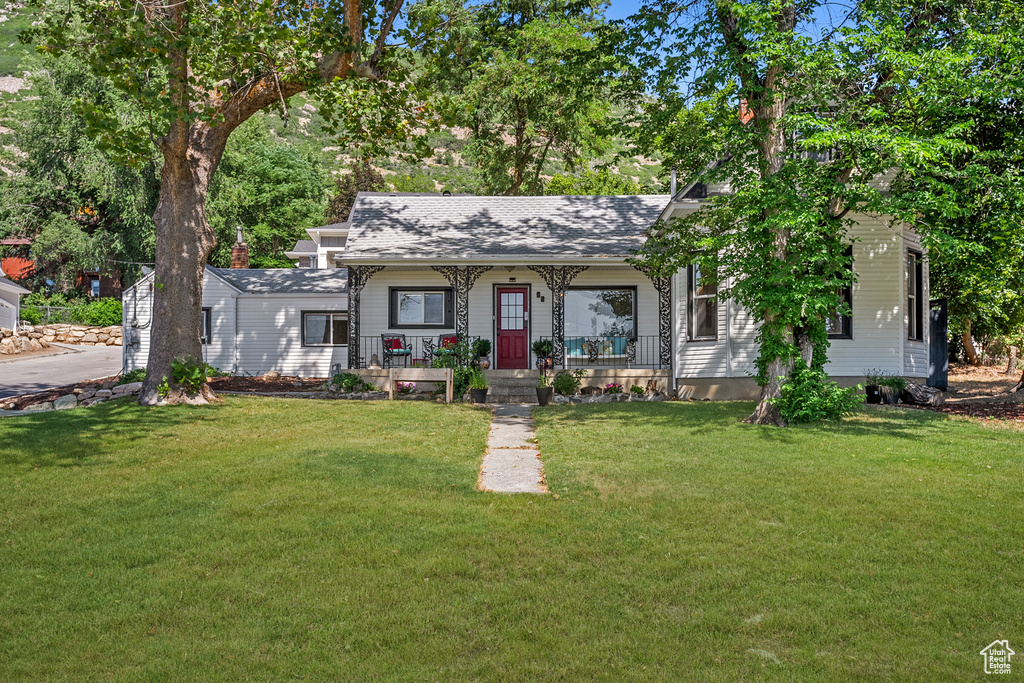 View of front of home with covered porch, roof with shingles, and a front lawn
