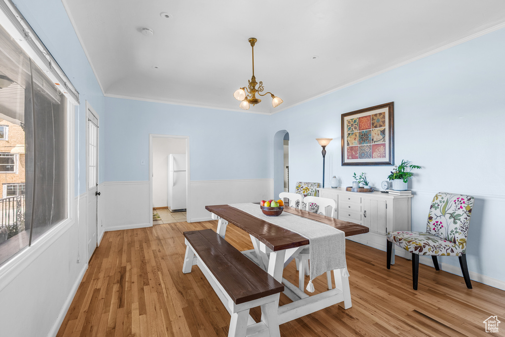 Dining area featuring arched walkways, crown molding, light wood finished floors, and a chandelier