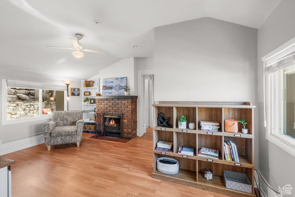 Living area featuring lofted ceiling, a ceiling fan, wood finished floors, a fireplace, and a baseboard heating unit