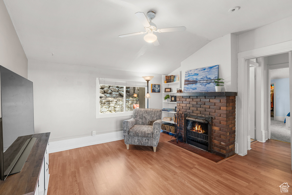 Sitting room featuring ceiling fan, vaulted ceiling, a fireplace, and light wood-type flooring