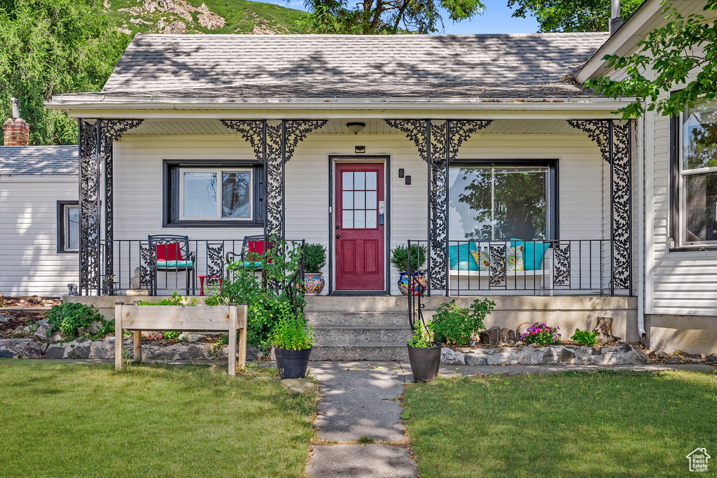 View of front of house with covered porch, a front lawn, and roof with shingles