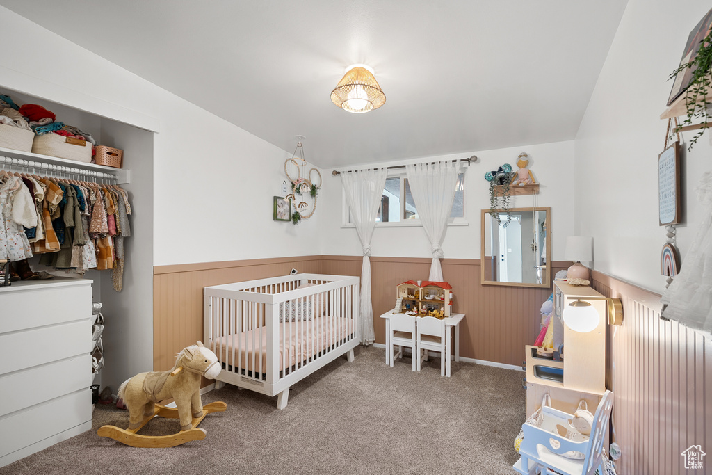 Carpeted bedroom with wainscoting, a nursery area, wood walls, and a closet