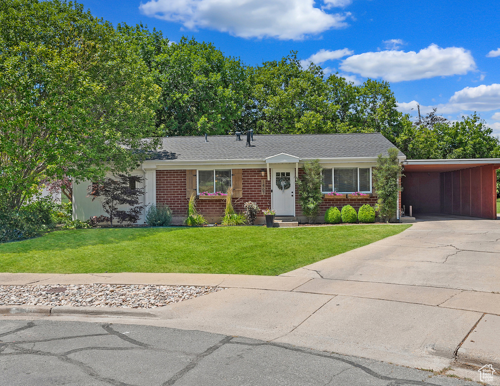 Ranch-style house featuring a front lawn, brick siding, driveway, an attached carport, and a shingled roof