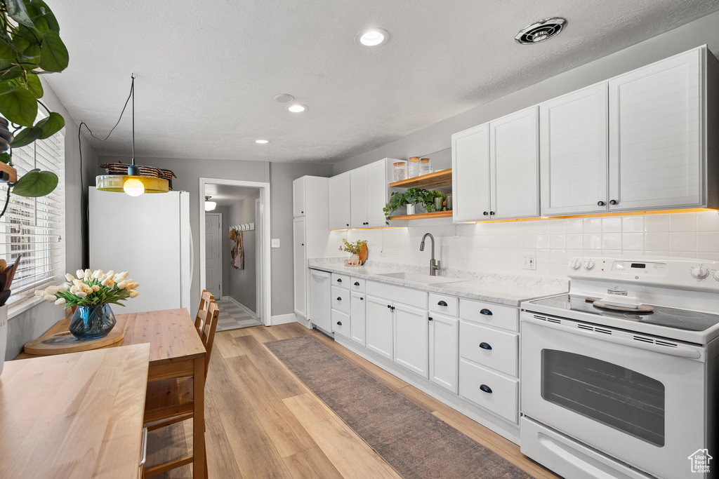 Kitchen with white appliances, open shelves, decorative backsplash, light wood-style flooring, and white cabinetry