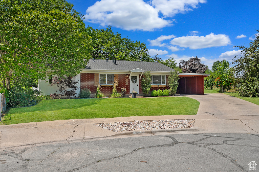 View of front of property with driveway, a front yard, a carport, brick siding, and a shingled roof