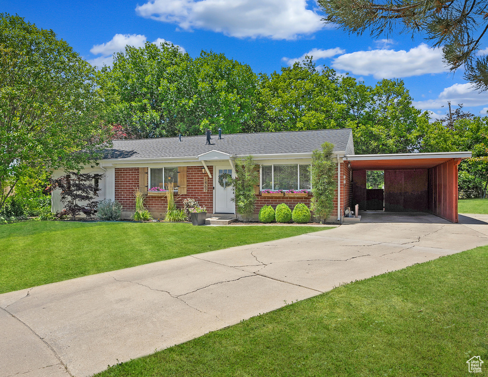 View of front of house featuring brick siding, driveway, a front yard, a carport, and roof with shingles