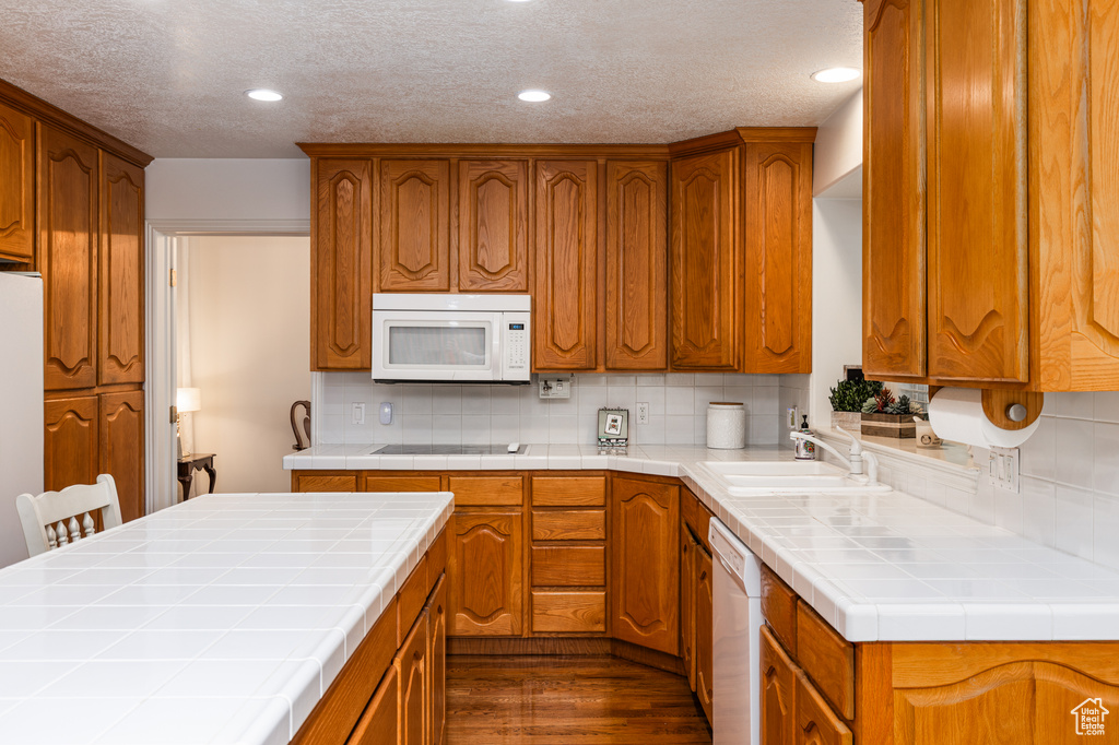 Kitchen featuring white appliances, tile counters, dark wood-style flooring, brown cabinets, and recessed lighting