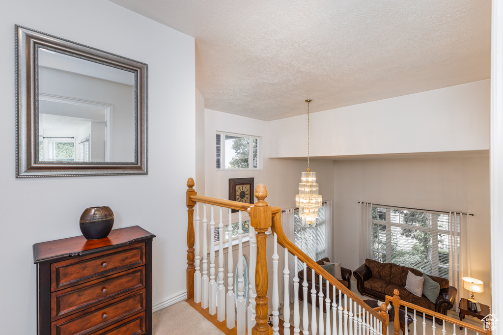 Corridor with an upstairs landing, a chandelier, carpet flooring, and a textured ceiling
