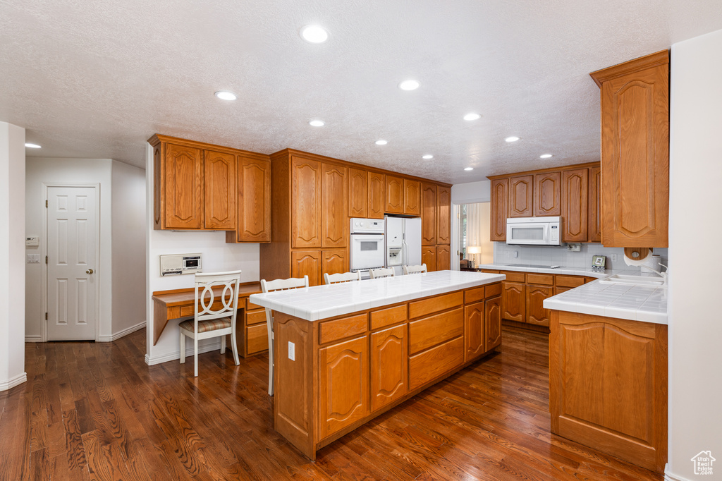 Kitchen featuring white appliances, a kitchen island, dark wood finished floors, recessed lighting, and brown cabinetry