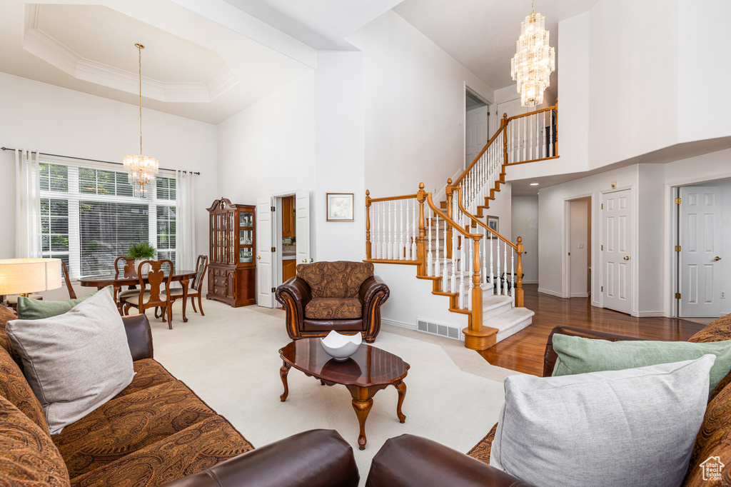Living room with a chandelier, a high ceiling, stairs, crown molding, and a raised ceiling