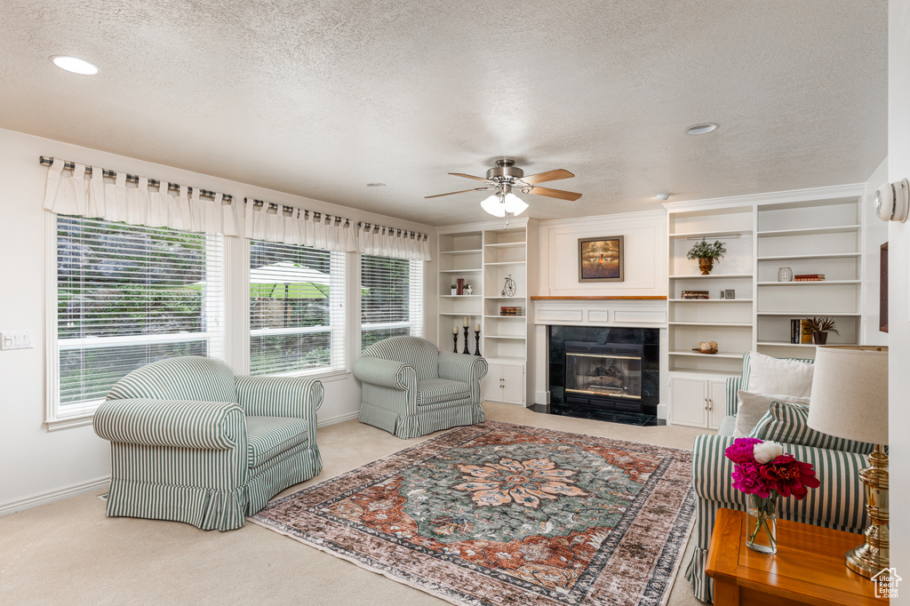 Living area with a textured ceiling, healthy amount of natural light, a ceiling fan, a fireplace, and carpet floors