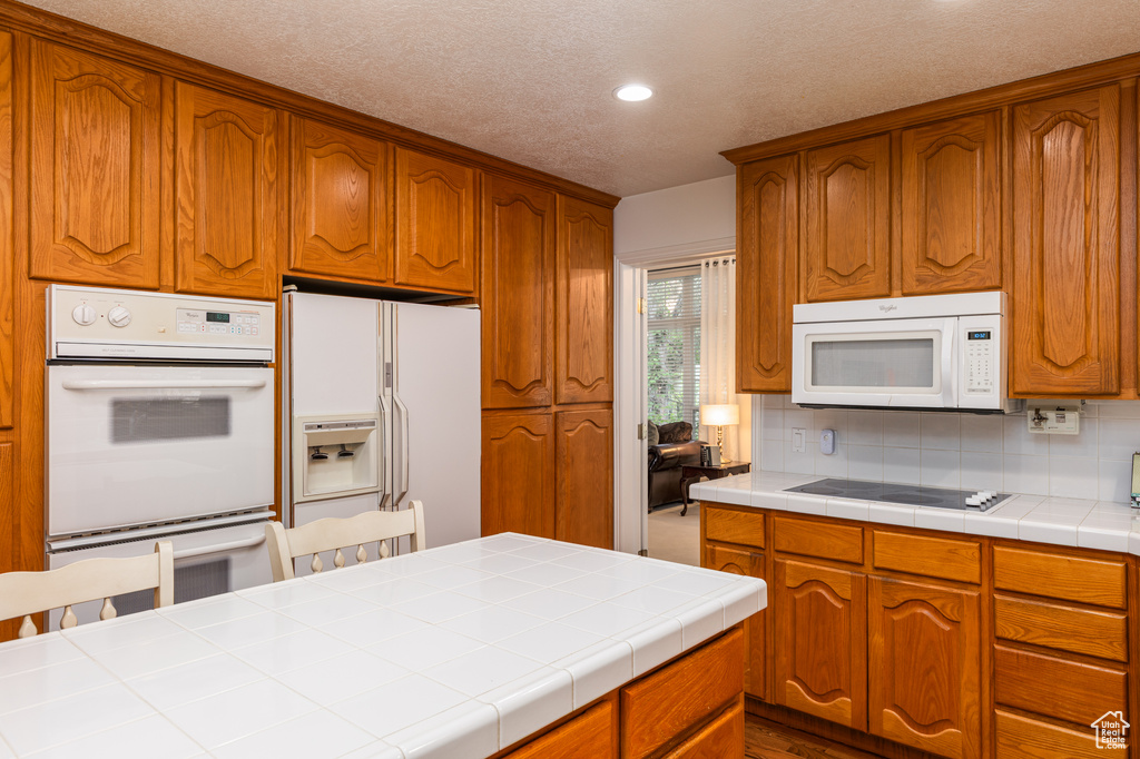 Kitchen featuring white appliances, recessed lighting, tasteful backsplash, brown cabinetry, and a textured ceiling