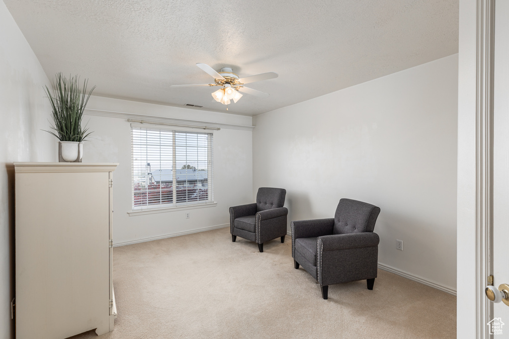 Sitting room featuring light colored carpet, ceiling fan, and a textured ceiling