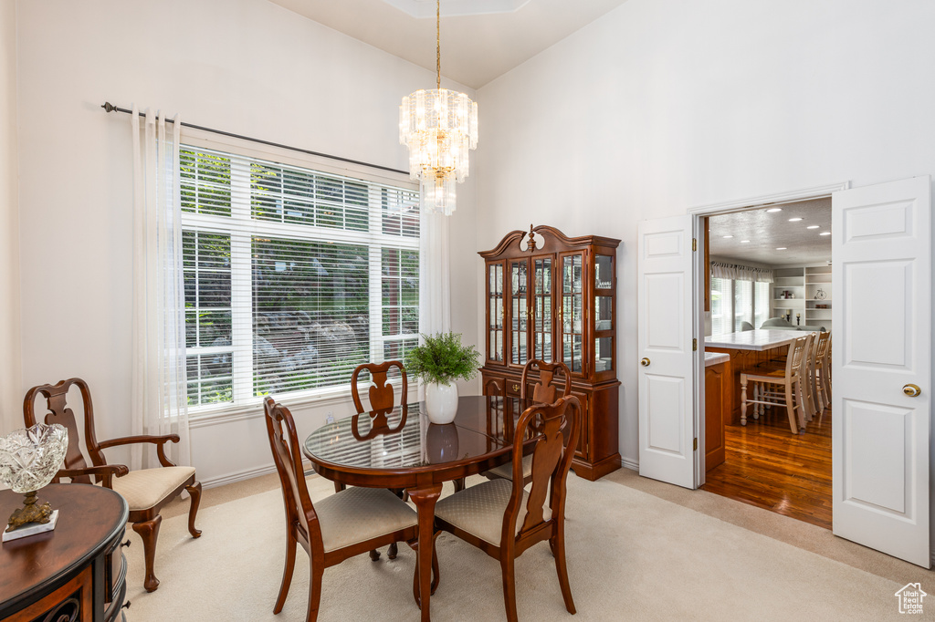 Dining area featuring high vaulted ceiling, light colored carpet, and a chandelier