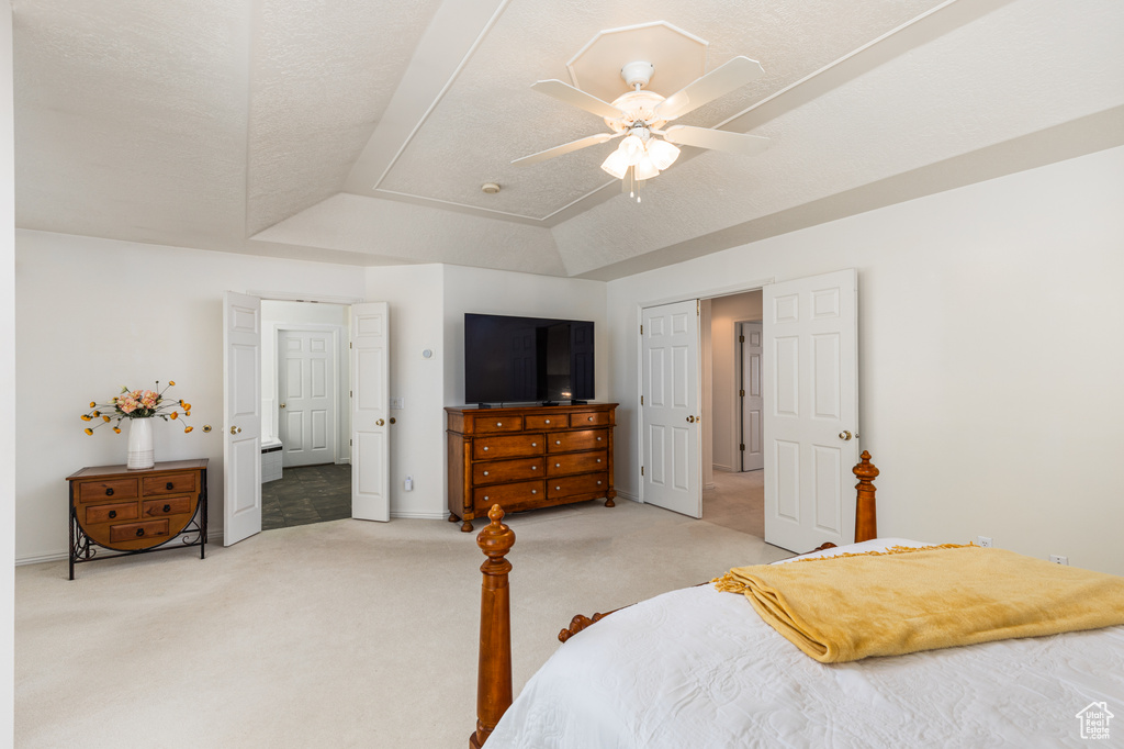 Bedroom with light carpet, a raised ceiling, and ceiling fan