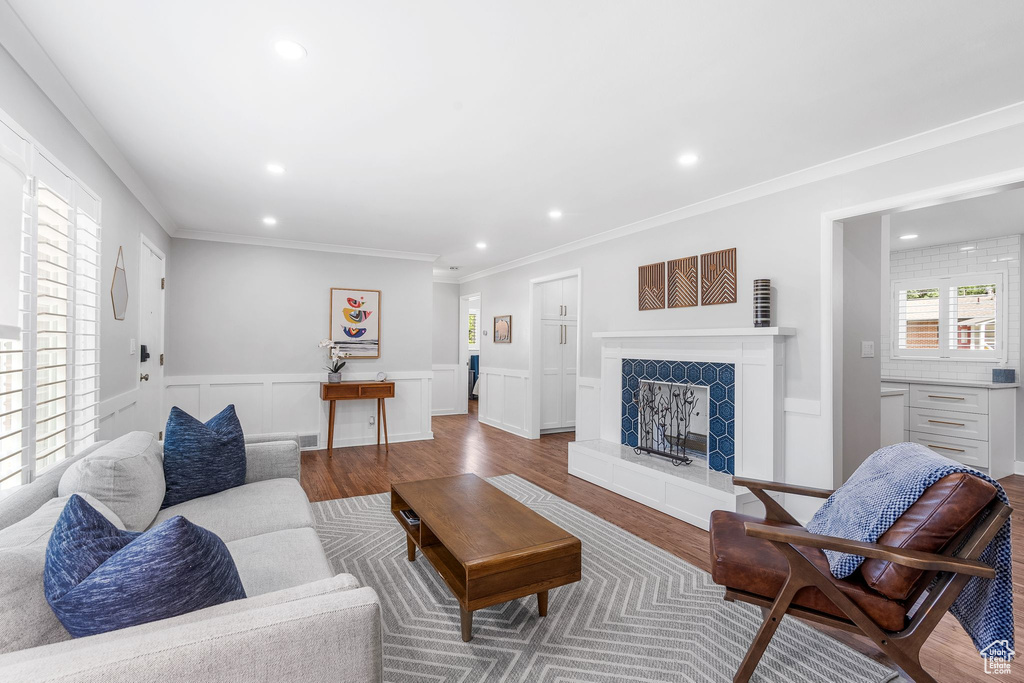 Living room featuring recessed lighting, a fireplace with raised hearth, wood finished floors, crown molding, and a wainscoted wall