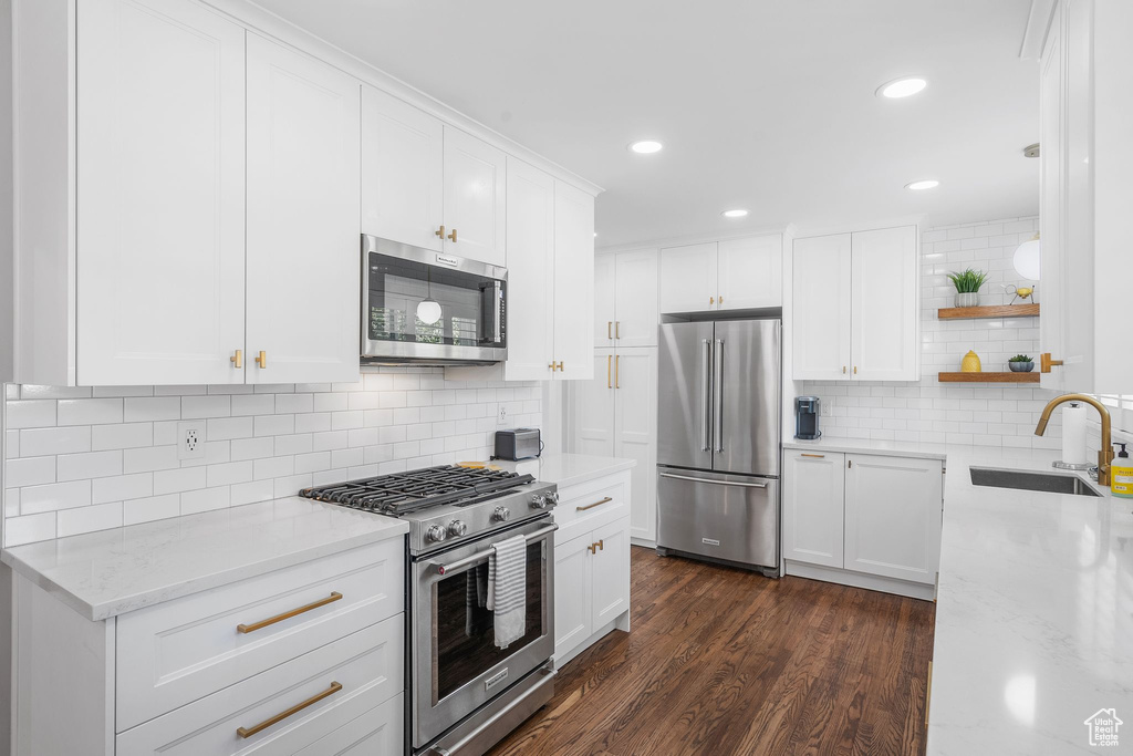 Kitchen featuring high quality appliances, open shelves, backsplash, white cabinetry, and dark wood finished floors