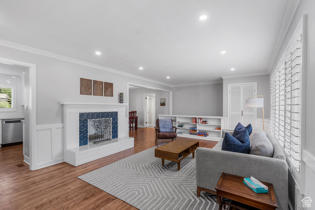 Living room with wood finished floors, a fireplace, recessed lighting, ornamental molding, and wainscoting