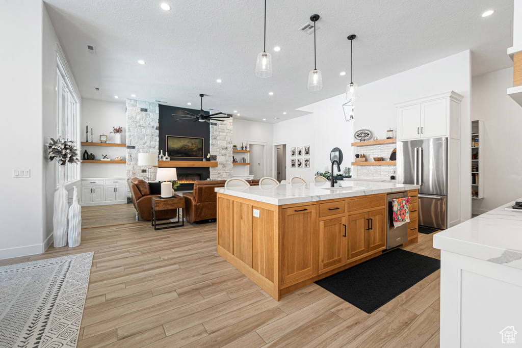 Kitchen featuring a large fireplace, ceiling fan, stainless steel appliances, light countertops, and light wood-style flooring
