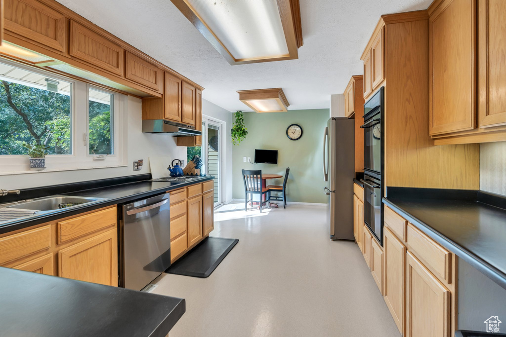 Kitchen featuring stainless steel appliances, dark countertops, finished concrete floors, and under cabinet range hood