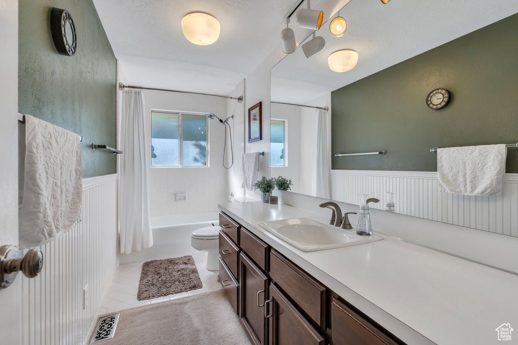 Full bathroom featuring vanity, shower / bathtub combination with curtain, a wainscoted wall, and tile patterned floors