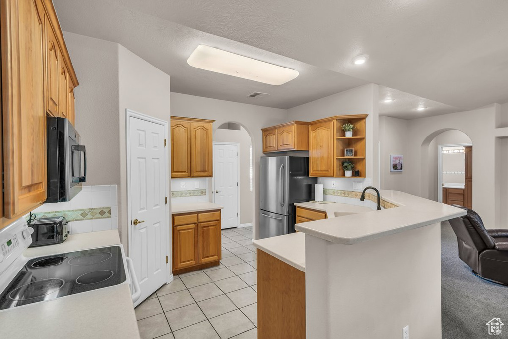 Kitchen featuring arched walkways, white electric range oven, freestanding refrigerator, light countertops, and a peninsula
