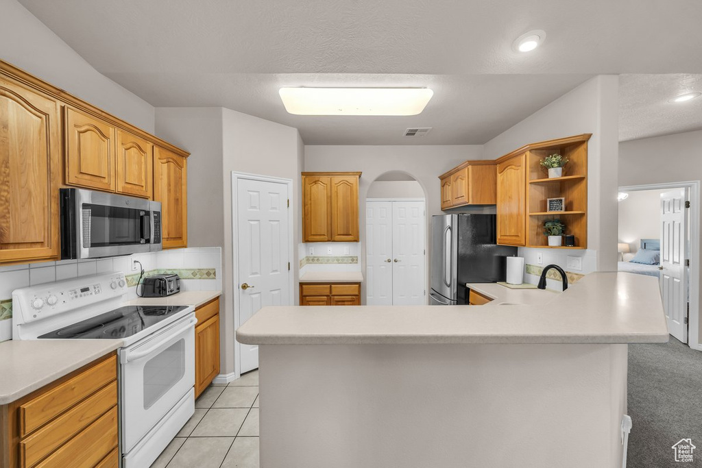 Kitchen featuring appliances with stainless steel finishes, open shelves, light countertops, a peninsula, and arched walkways