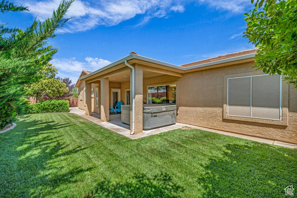 Back of property featuring stucco siding, a patio, a hot tub, and a lawn