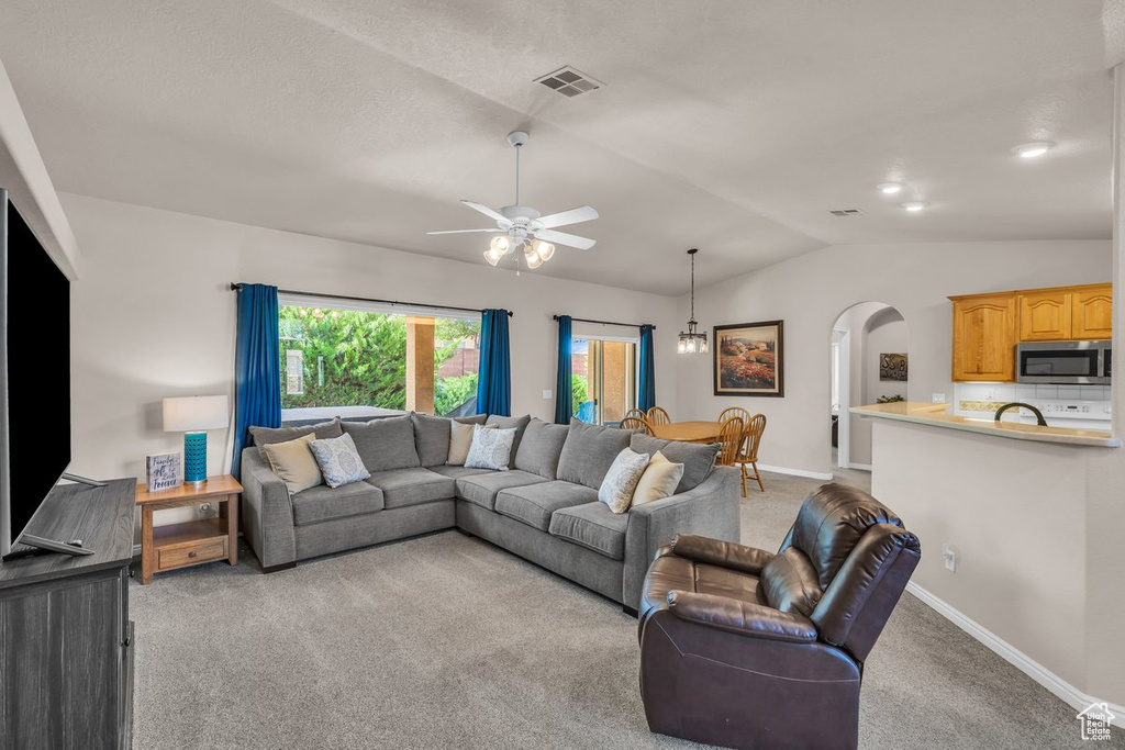 Carpeted living room with arched walkways, lofted ceiling, and a ceiling fan