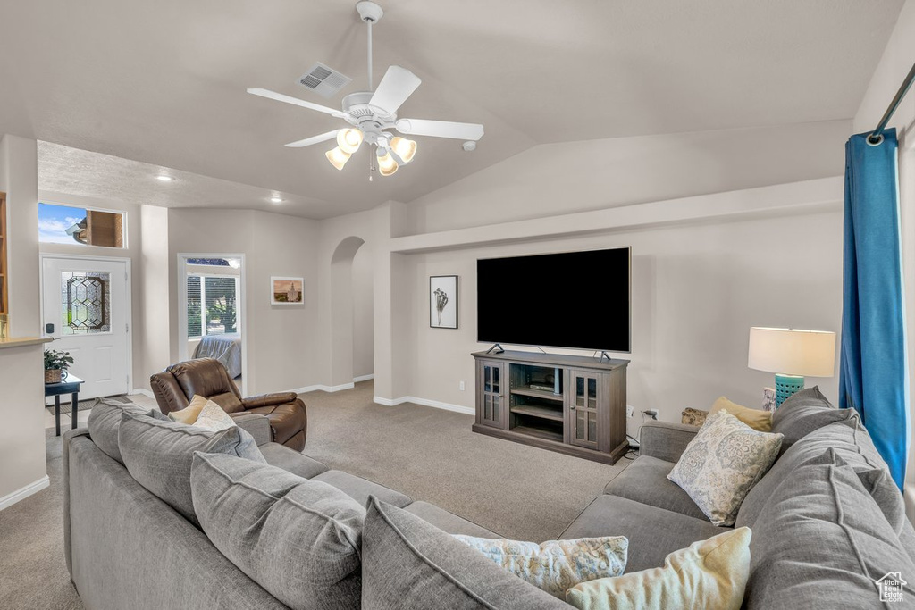 Carpeted living area with arched walkways, vaulted ceiling, and ceiling fan