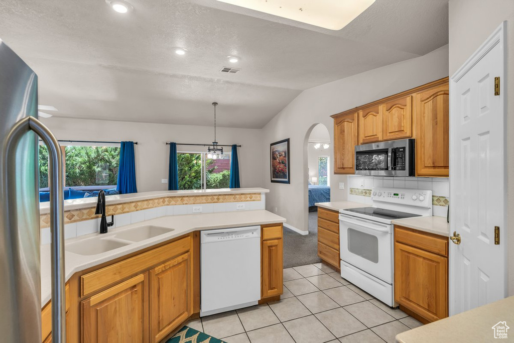 Kitchen with stainless steel appliances, vaulted ceiling, decorative backsplash, light countertops, and arched walkways